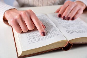 Fototapeta premium Female hands with brown nails polish color and finger on an open book. Manicure and beauty concept