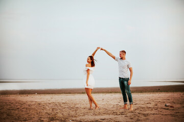 A guy in jeans and a grey t-shirt holding hand dancing women in white dress 