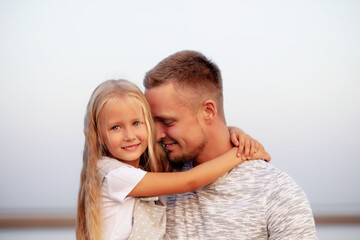 A father holds a small blonde daughter with blue eyes in his arms