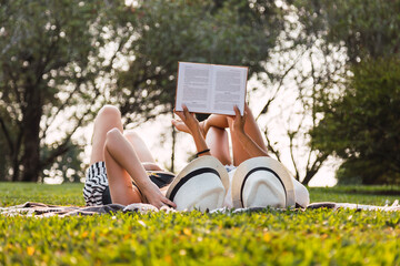 Young friends read at the outdoor. Friends lying down, reading a book. Two friends with hats read a...