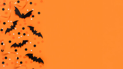 Bats and celebration decorations on orange background, top view with copy space. Halloween creative...