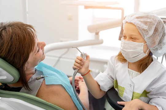 Caucasian seven year old girl playing at a dentist. Child holding dental instruments in hands, woman dentist depicts a patient