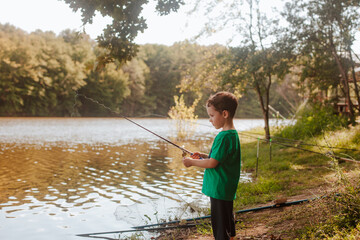 A small beautiful boy in a green t-shirt fishing on a fishing rod on the coast river. 
