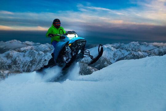 Adventurous Man Riding a Snowmobile in white snow during a colorful sunset. Epic Action Image Composite. Background from British Columbia, Canada.