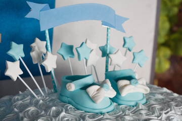 Cream and cream fondant cake with shoes with bows and buttons and stars for party or child christening celebration.