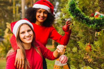 Young friends at the Christmas tree. Multiracial friends in the park. Friends decorating the Christmas tree. Concept of Christmas and friendship.