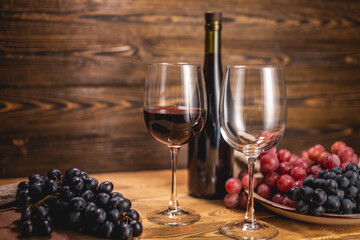 Bottle of dry red wine with a glass and a bunch of grapes on a wooden table. Concept of viticulture and winemaking