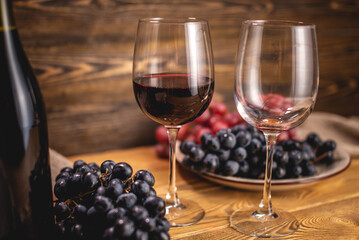 Bottle of dry red wine with a glass and a bunch of grapes on a wooden table. Concept of viticulture and winemaking