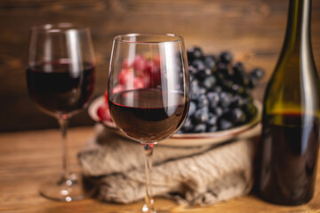 Bottle of dry red wine with a glass and a bunch of grapes on a wooden table. Concept of viticulture and winemaking