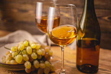 Bottle of dry white wine with a glass and a bunch of grapes on a wooden table. Concept of viticulture and winemaking