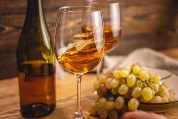 Bottle of dry white wine with a glass and a bunch of grapes on a wooden table. Concept of viticulture and winemaking
