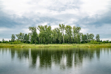 summer landscape of the forest by the lake with clouds in the sky and a little rain