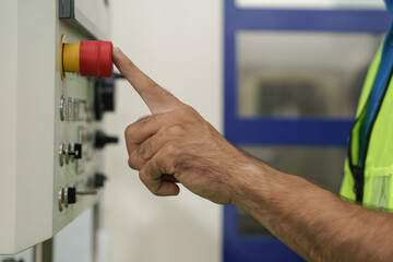 closeup of finger pressing red button on cnc machine control panel at factory
