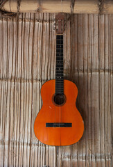 Fototapeta premium orange acoustic guitar with strings hanging on a reed wall, closeup to the parts of the musical instrument
