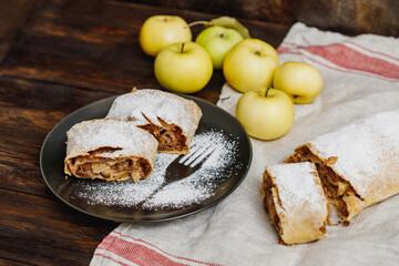 Apple strudel with icing sugar and raisins on black plate