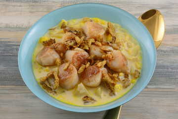 Spicy chowder soup with scallops potatoes and corn and crispy jalapeno pepper topping in blue bowl with golden soup spoon