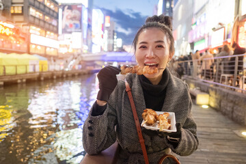 Young woman tourists enjoy eating street food in walking at street shopping center Dotonbori in Osaka, Japan.