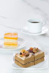 Coffee cake and orange soft fudge cake with black coffee on white marble table in vertical frame, selective focus 