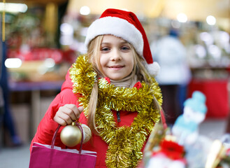 Cute little girl in Santa hat shopping decorations on traditional Christmas market