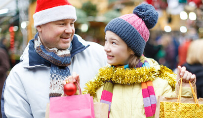 Preteen girl with her father looking happy with shopping bags on outdoor Christmas fair..