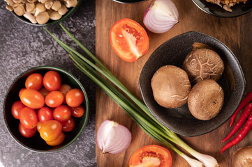 Shiitake mushrooms with garlic, tomato, capsicum, spring onion and red onions on a black cement floor.