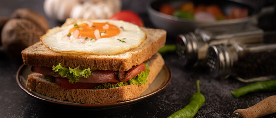 Breakfast sandwich made with bread, fried egg, ham, and lettuce.