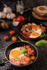 Fototapeta na wymiar Breakfast with fried eggs, sausage, and ham in a pan with tomatoes. Chili and basil.