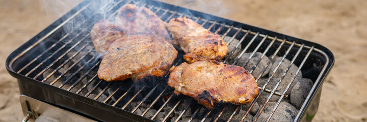 Steak on compact charcoal grill for travel in the cooking process.