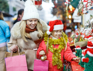 Smiling cute preteen girl having fun on Christmas fair with mother, selecting decoration for home
