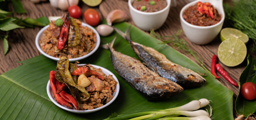 Shrimp paste, mackerel, fried on banana leaves, chili, tomato, garlic and lemon on wooden floor.