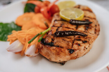 Chicken Steak with Lemon, Tomato, Chili, and Carrot on White Plate.
