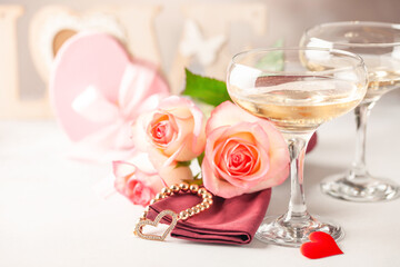 Champagne glasses, a bouquet of roses and a gift on a bright background. Romantic celebration of Valentine's day
