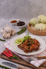 Sweet pork on a white plate with chopped scallions, chili, lime, cucumber, tomato, and garlic.