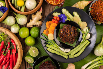 Chili paste is served on banana leaves on a plate with long beans, lime, chili, and eggplant.
