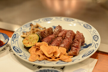 Premium Kobe Beef Steak in a white plate with fried garlic and grilled vegetables. In a teppanyaki shop in Kobe, Japan