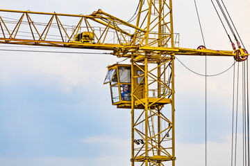 Partial view of a yellow tower construction crane - Operating cabin with operator inside it.