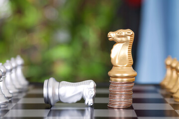 A golden horse chess piece standing on a stack of dollar coins and a silver horse chess piece...