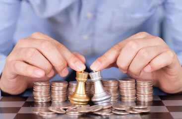 Two hands next to the dollar coin help two chess rooks duel