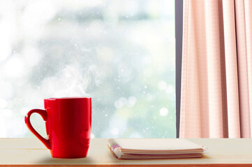 Hot coffee on wooden table and falling snow outside the window