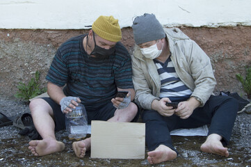 Fototapeta na wymiar Two homeless people sit on the street in medical masks, begging. COVID-19 . Poverty, unemployment, alcoholism.