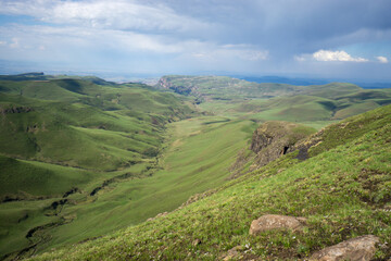 Obraz premium Valley in the Drakensberg mountains clad in green summer grass with an approaching thunderstorm in the distance.