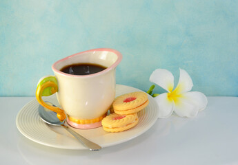 Breakfast, coffee, cookies, spoon, flowers placed on a white tile table.