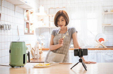 Portrait of beauty asian woman review cooking fry potato food , recording live video using air flyer smart device at home. Online influencer girl on social media marketing, hobby and leisure concept