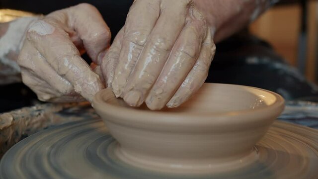 Close-up of adult man's hands shaping clay into beautiful hand-made bowl on throwing-wheel working alone in studio. People and creativity concept.
