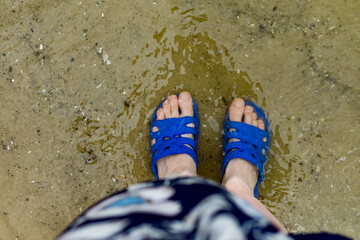 Women's feet feet and fingers in blue rubber flip-flops, Slippers, are submerged in salty sea water near the shore, on smooth stone pebbles in Sunny weather