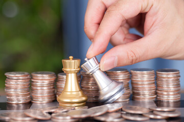 In front of a large number of dollar coins, one hand helps the silver chess piece to defeat the...