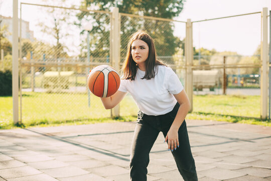 Young cute teen girl leads the ball in a basketball game. A girl plays basketball after school. Sports, healthy lifestyle, leisure