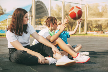 Cheerful high school students sit on the basketball court, relax after the game, talk and laugh. Sports, games, and education. The concept of friendship