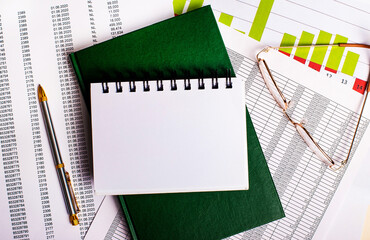 Glasses, a pen and a green diary with a business card lie on the desktop against the background of...