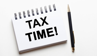 On a light background, a white notebook with the words TAX TIME and a pen. Tax concept